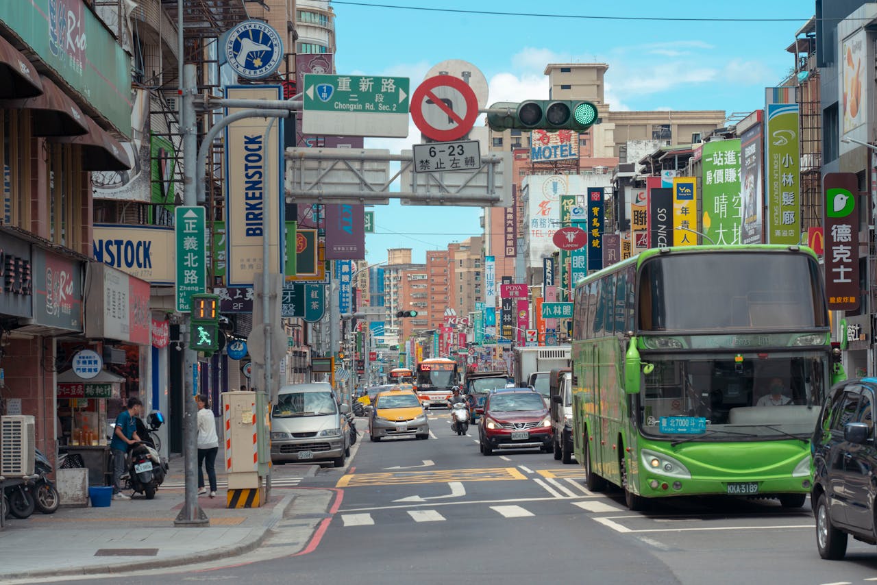 Busy urban street in Taipei with colorful signs, buses, and pedestrians under bright daylight.